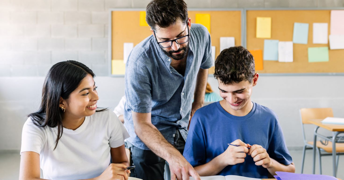 A teacher helps two teenage students read the text of their book