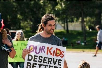 Martin Plemel holding sign "our kids deserve better"