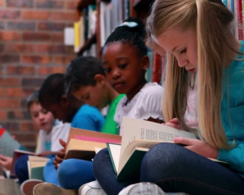Group of diverse children reading books together at the library