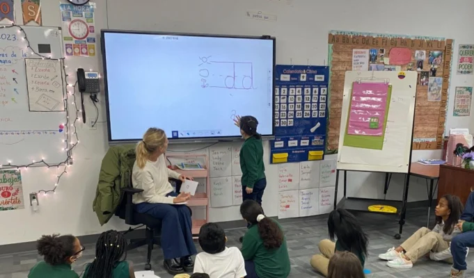 child pointing at whiteboard with teacher and class looking